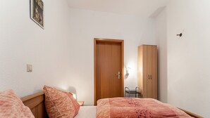 A bedroom with two beds, a wooden wardrobe, a small table, and a door. - Home for 5 Persons in 1350 Year Old Mosel Town (Ediger-Eller)