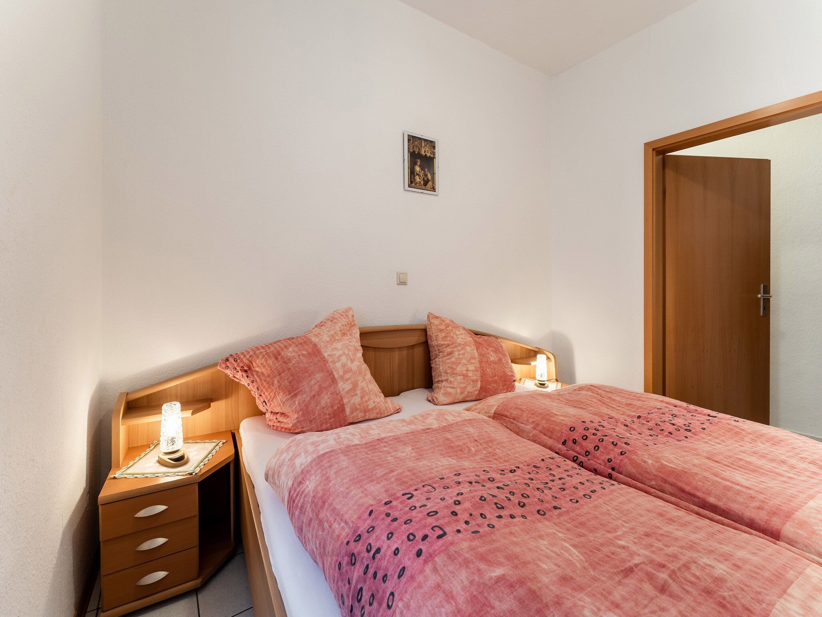 Un dormitorio con una cama, dos mesitas de noche, un cabecero de madera, un cuadro en la pared y una puerta.