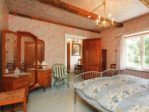 Una habitación con papel tapiz floral, una cama de madera, una silla verde, un aparador y un espejo.