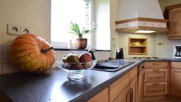 A kitchen with a large pumpkin, a bowl of fruits, and a potted plant on the counter.