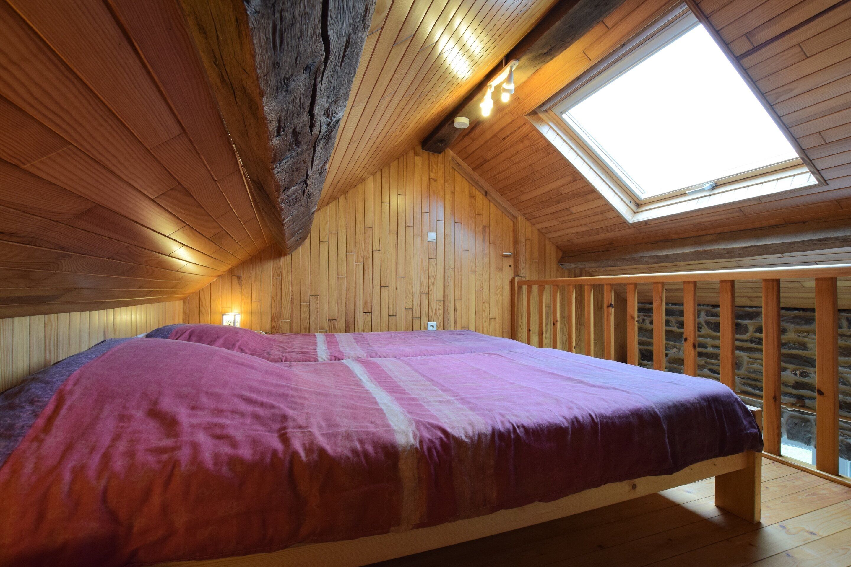 A wooden interior with a bed, a skylight, and stone walls.