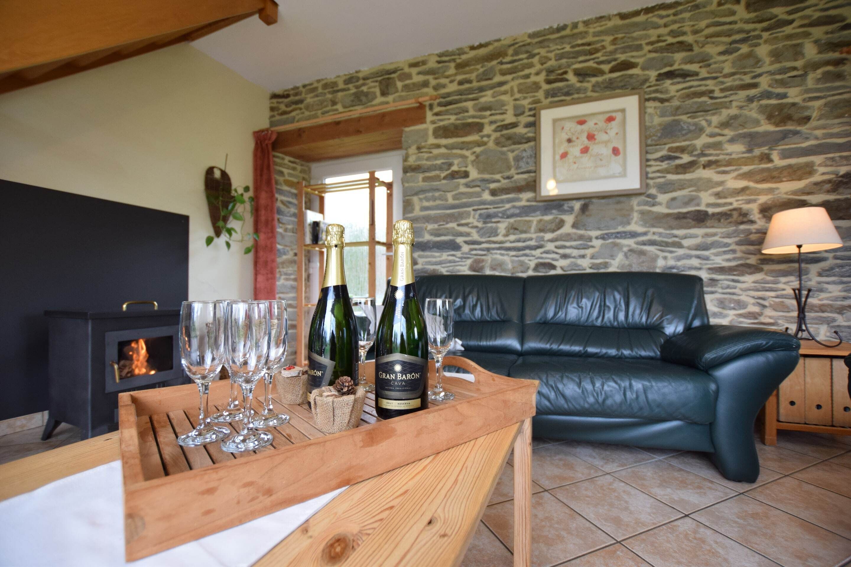 Una sala de estar acogedora con una pared de piedra, una chimenea negra, un sofá de cuero y una mesa de madera con botellas de vino y copas.