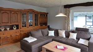 A living room with a brown sofa, a wooden cabinet, and a window with curtains. - Geraumige Ferienwohnung im Sauerland (Olsberg)