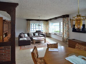 Ein Wohnzimmer mit Ecksofa, Couchtisch, Esstisch mit Stühlen und einem großen Fenster mit Vorhängen.