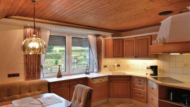 A kitchen with wooden cabinets, a dining area with a table and chairs, and a window with curtains. - Geraumige Ferienwohnung im Sauerland (Olsberg)