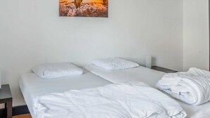 Een tweepersoonsbed met witte beddengoed en kussens, een houten nachtkastje en een schilderij van een woestijnlandschap aan de muur.