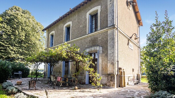 A two-story stone building with a tiled roof, a covered patio with outdoor furniture, and a garden with trees and shrubs. - Former Train Station With Private Heated Swimming Pool & Fantastic Garden (Liglet)