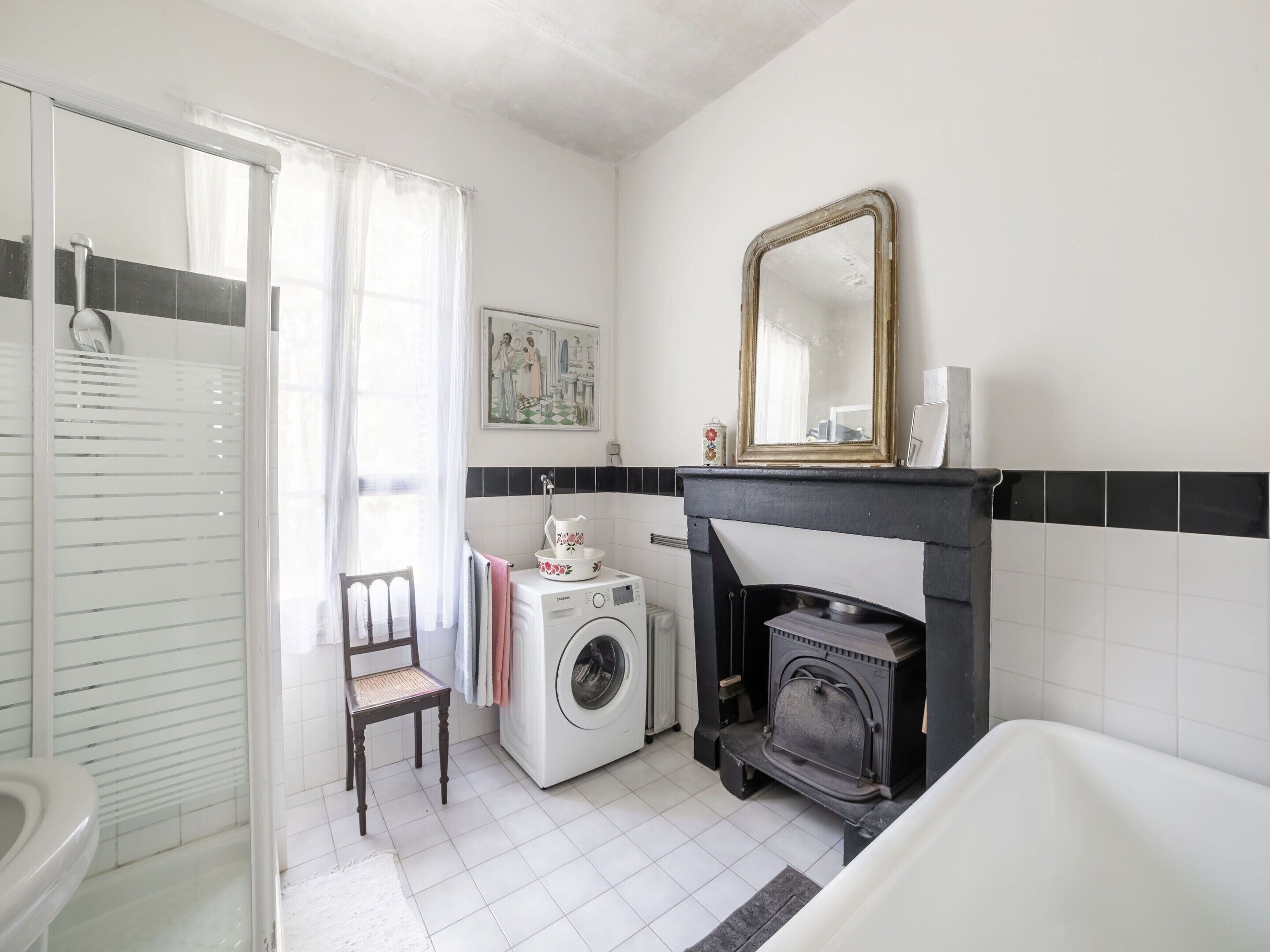 A bathroom with a washing machine, a fireplace, a mirror, and a chair.