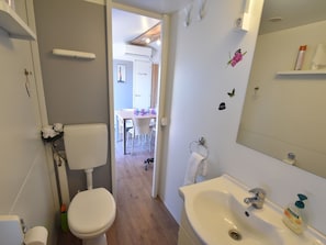 Een badkamer met toilet, wastafel en spiegel. Een douchegedeelte is zichtbaar op de achtergrond.