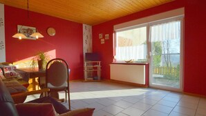 A living room with a red wall, a wooden ceiling, a sofa, a table with a plant, and a window with a view.