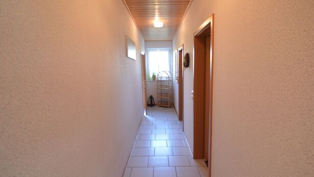 A narrow hallway with white tiled flooring and wooden ceiling beams.