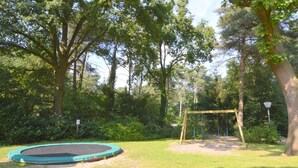 A playground with a trampoline and a swing set in a wooded area.