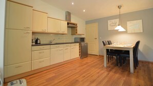 A kitchen with wooden cabinets, a microwave, and a dishwasher. There is a dining table with chairs and a hanging light fixture.