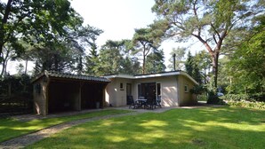 A single-story house with a covered porch, a small patio with a table and chairs, and a well-maintained lawn.