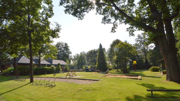 A park with picnic tables, a playground, and a building in the background.