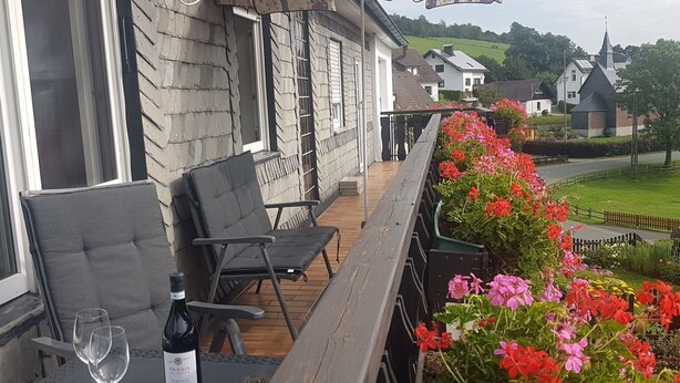 A balcony with two chairs, a table, and a bottle of wine.