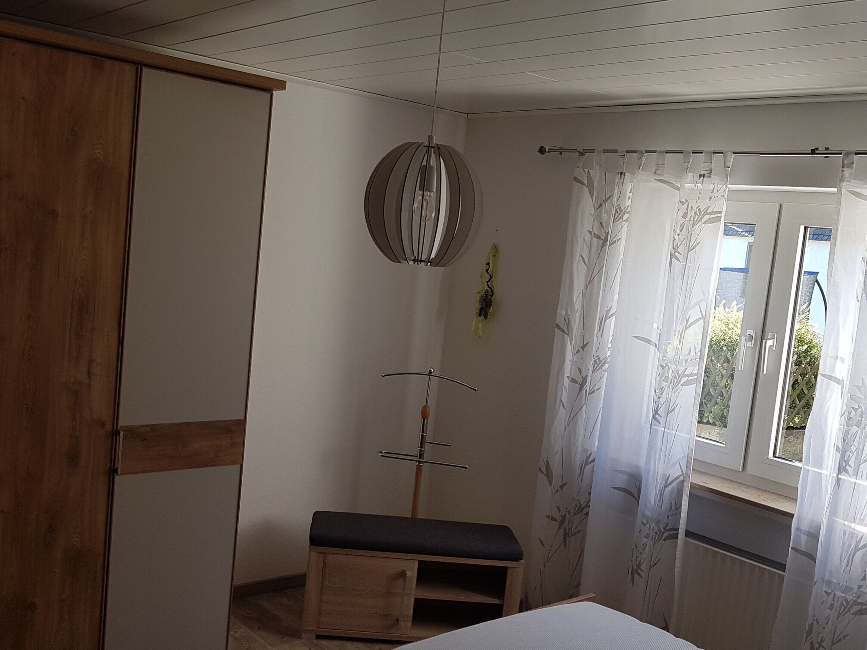 Ein Schlafzimmer mit einem Holzschrank, einer Bank, einer Wandleuchte und einem Fenster mit Bambusvorhang.