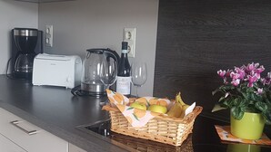 A kitchen with a toaster, coffee maker, kettle, wine glass, and a basket of fruit.