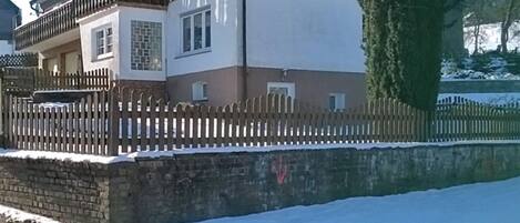 A two-story house with a balcony, a stone wall, and a wooden fence.