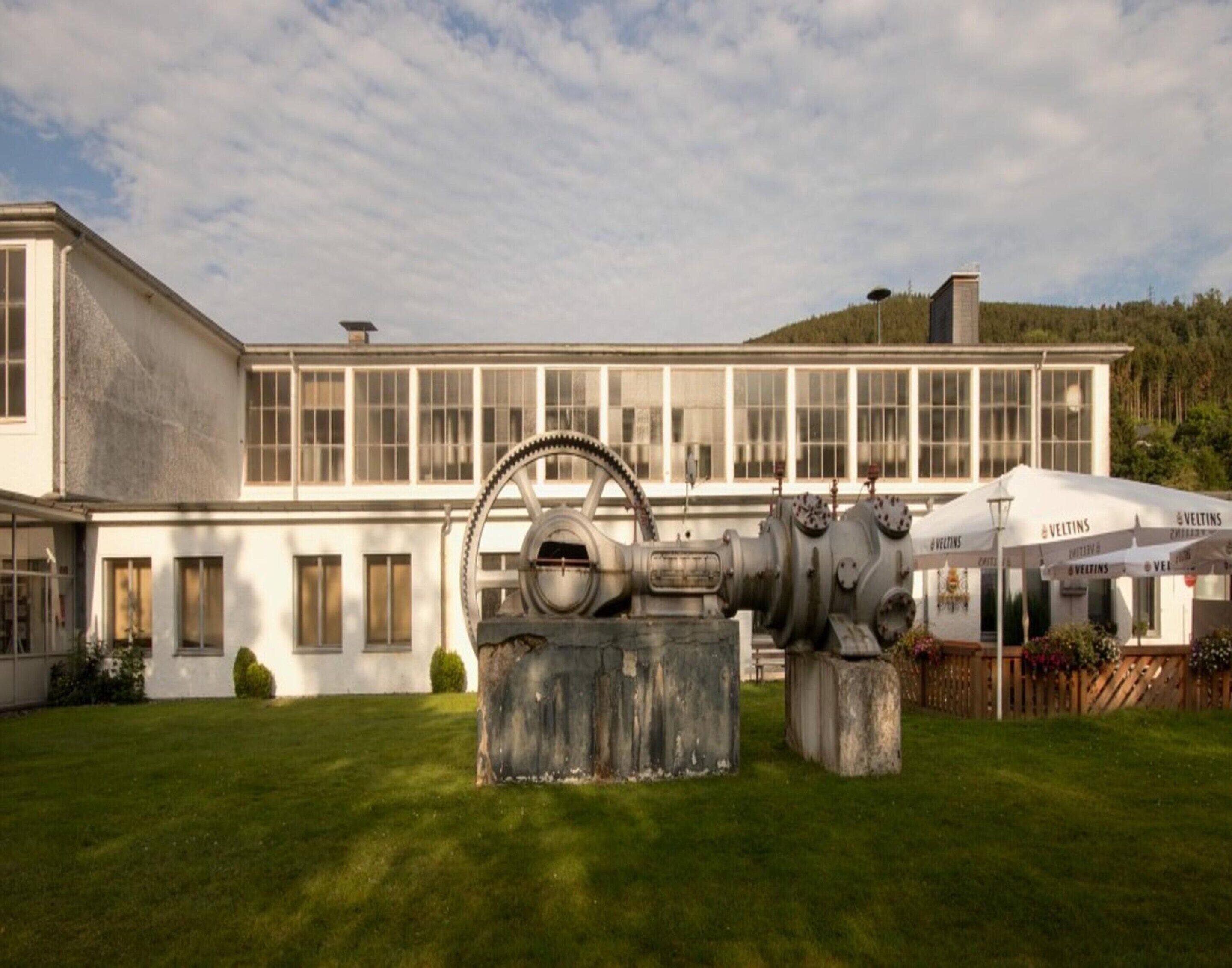 A building with large windows, a grassy lawn, and outdoor seating with umbrellas.
