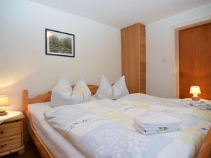 Una cama bien tendida con ropa de cama y almohadas estampadas con motivos florales, un cabecero de madera, una mesita de noche con una lámpara y un cuadro en la pared.