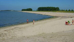 En strand med klare himmel, roligt vand og et par personer.