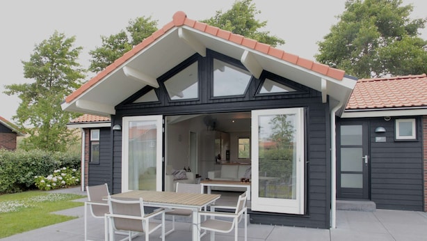 Et moderne hus med terrasse, spisebord og stole.