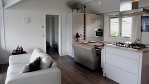 Et moderne køkken med en central ø, et spiseområde med et hvidt bord og stole, og en opholdsstue med en hvid sofa.
