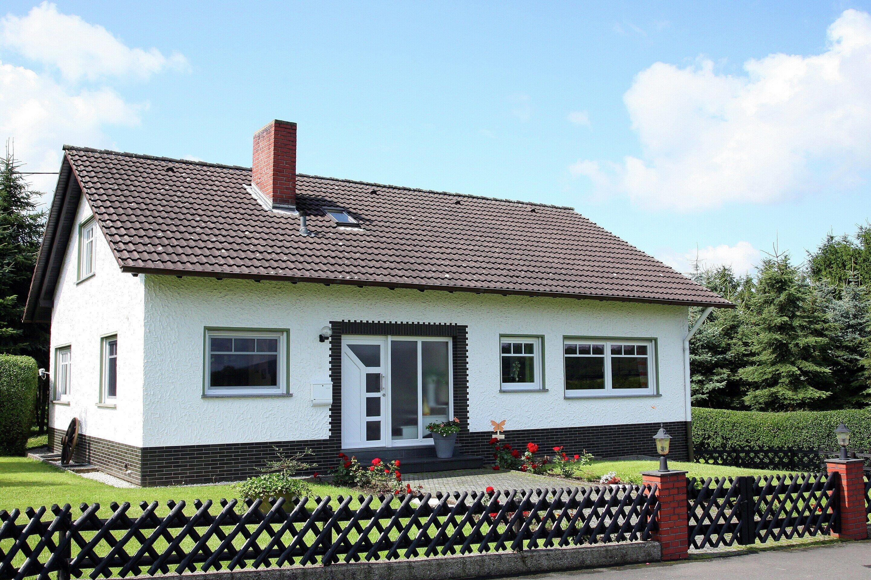 A two-story house with a tiled roof, a front door, and a small porch with a potted plant.
