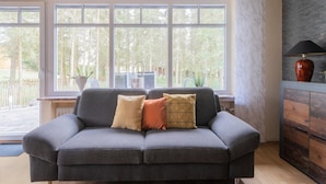 A modern living room with a grey sofa, a wooden cabinet, and a large window with a view of trees. - Trierscheid Countryside Escape (Trierscheid)