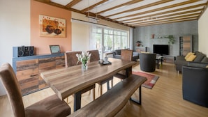 A spacious living area with a wooden dining table, comfortable seating, a fireplace, and a large window providing natural light. - Trierscheid Countryside Escape (Trierscheid)