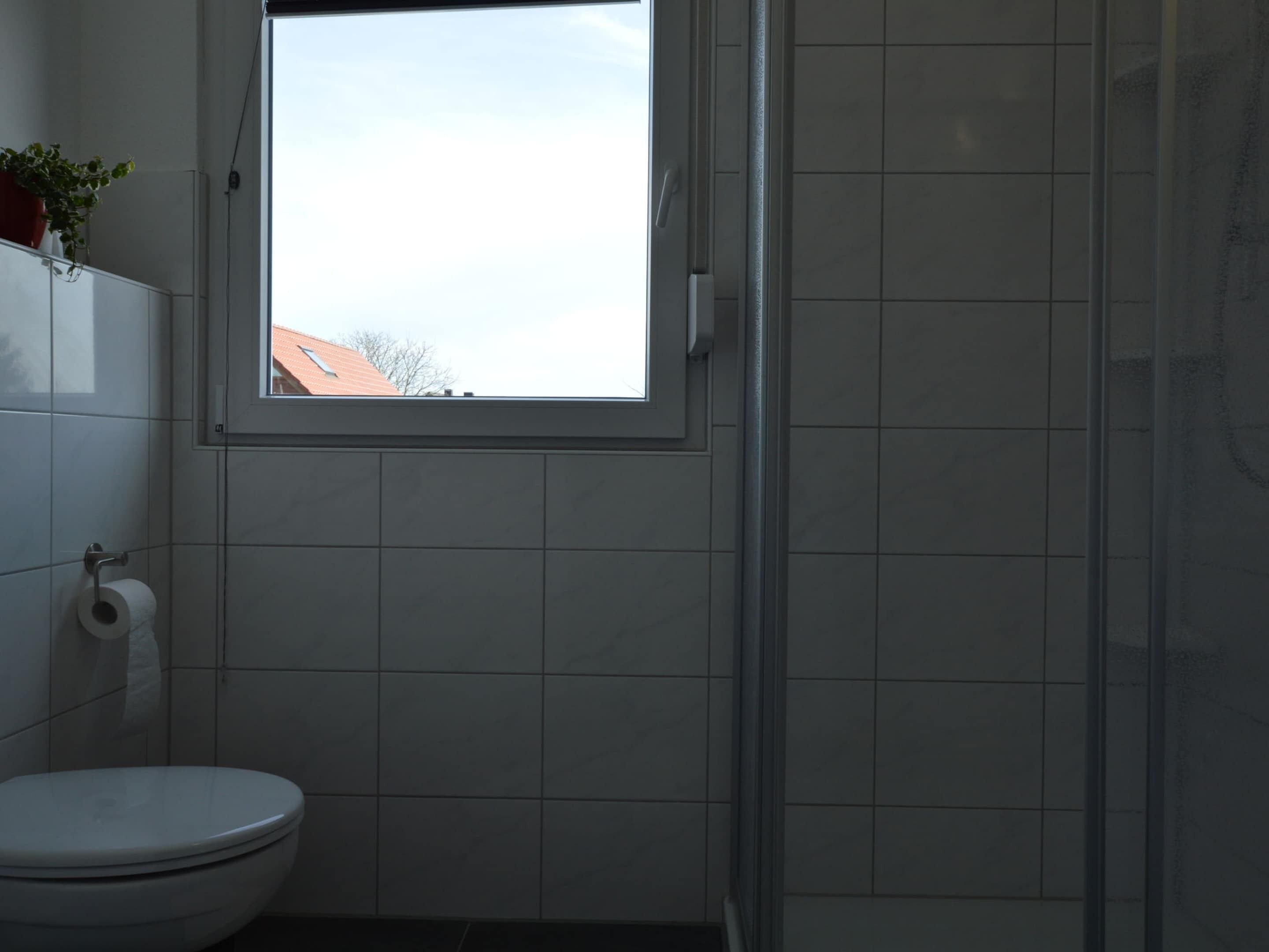 Une salle de bain comprenant des toilettes, une fenêtre et un espace douche.