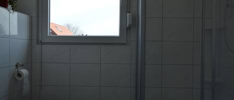 Une salle de bain comprenant des toilettes, une fenêtre et un espace douche.