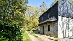 Un bâtiment en pierre de deux étages, avec un toit sombre, une allée gravillonnée et une haie verdoyante et luxuriante.