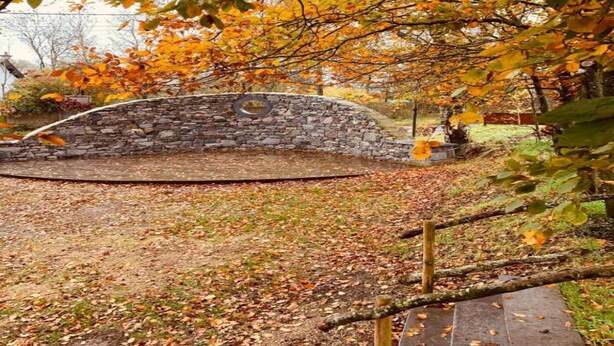 Une arche en pierre dans un parc, avec un mur en pierre et un banc en bois.