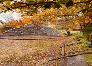 A stone archway in a park with a stone wall and a wooden bench.