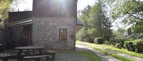 A stone building with a small window and a door, surrounded by a gravel area with picnic tables.