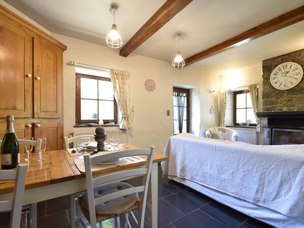 A cozy room with a wooden dining table, chairs, a bed with a white bedspread, a stone fireplace, and a large wall clock.