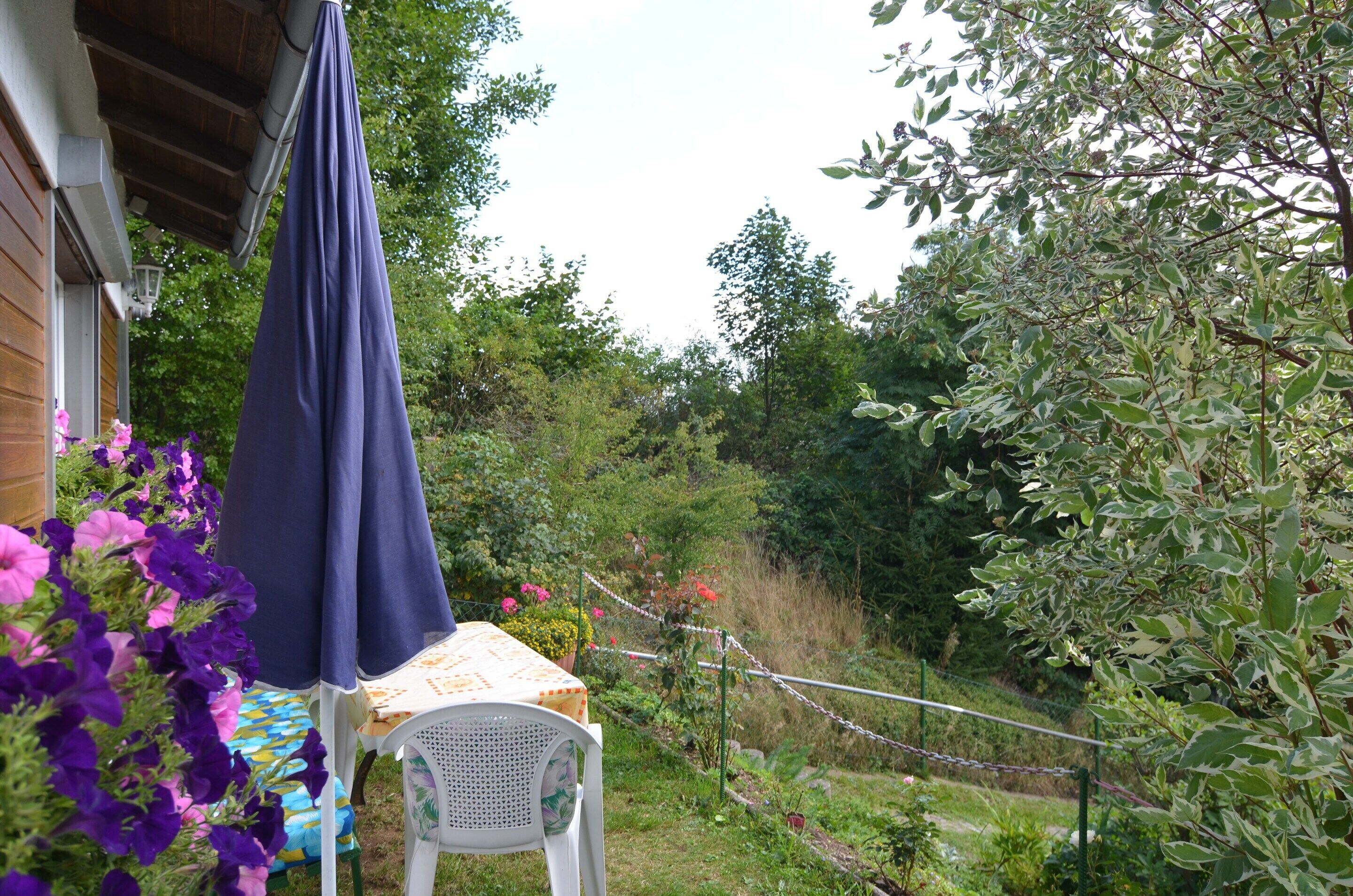 Um jardim com mesa e cadeiras, cercado por vegetação e flores.