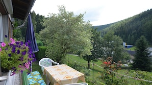 Un balcon agrémenté d’une table et de chaises, entouré de verdure et offrant une vue sur une vallée boisée.