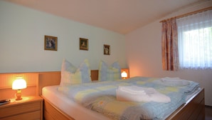 Un lit bien fait, recouvert d’une couverture à rayures, avec deux lampes de chevet et trois tableaux encadrés accrochés au mur.