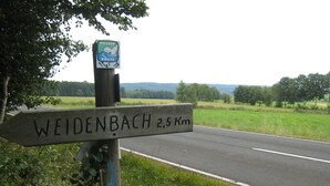 Puisesta opastekyltistä näkyy teksti ”WEIDENBACH 2,5 km” ja kyltti, jossa lukee ”WASSER ROUTE”.
