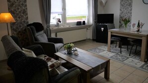 A living room with a sofa, a coffee table, a TV, and a dining area with a table and chairs. - Cozy Apartment in Strotzbüsch near Eifel Center (Strotzbusch)