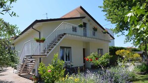 Een huis met twee verdiepingen, een balkon, een trap en een tuin met verschillende planten en bloemen.