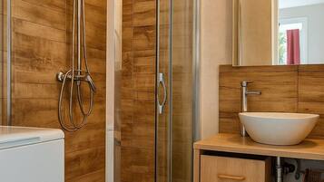 Un baño moderno con ducha envuelta en vidrio, tocador de madera con lavamanos y un espejo grande.