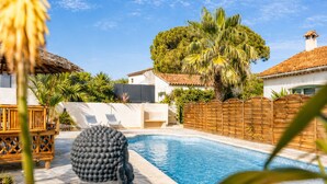 Una piscina con muelle de madera, una estatua y un área vallada con árboles y un edificio al fondo.
