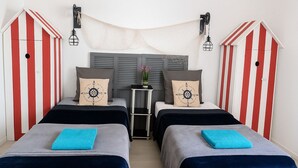 Una habitación con dos camas, cada una con una toalla azul, una mesita con una planta y paredes a rayas.
