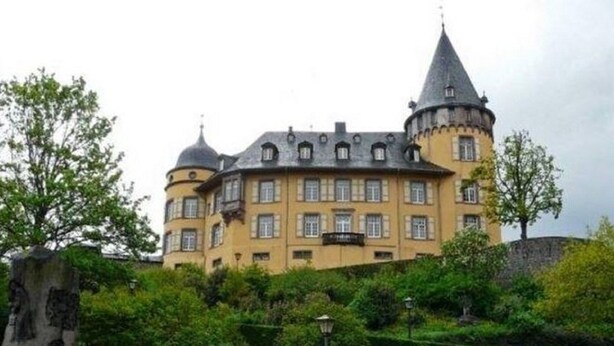 Un grand bâtiment historique doté de nombreuses tours et d’une tourelle, entouré d’une végétation luxuriante et d’un jardin bien entretenu.
