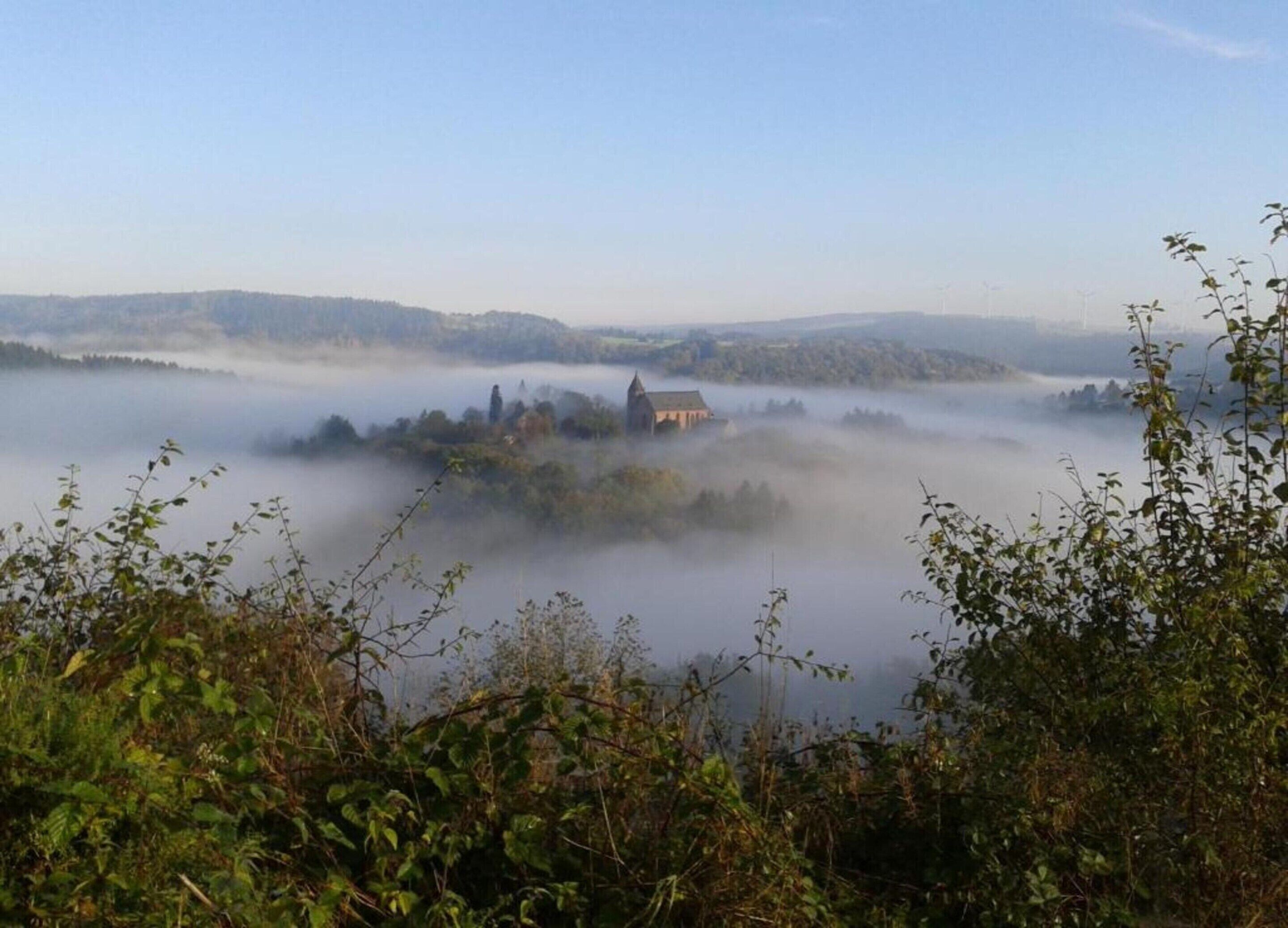 A misty landscape with a building surrounded by dense fog, likely a historic or rural location.