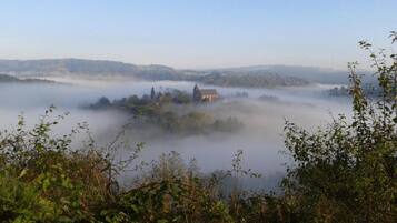 A misty landscape with a building surrounded by dense fog, likely a historic or rural location.